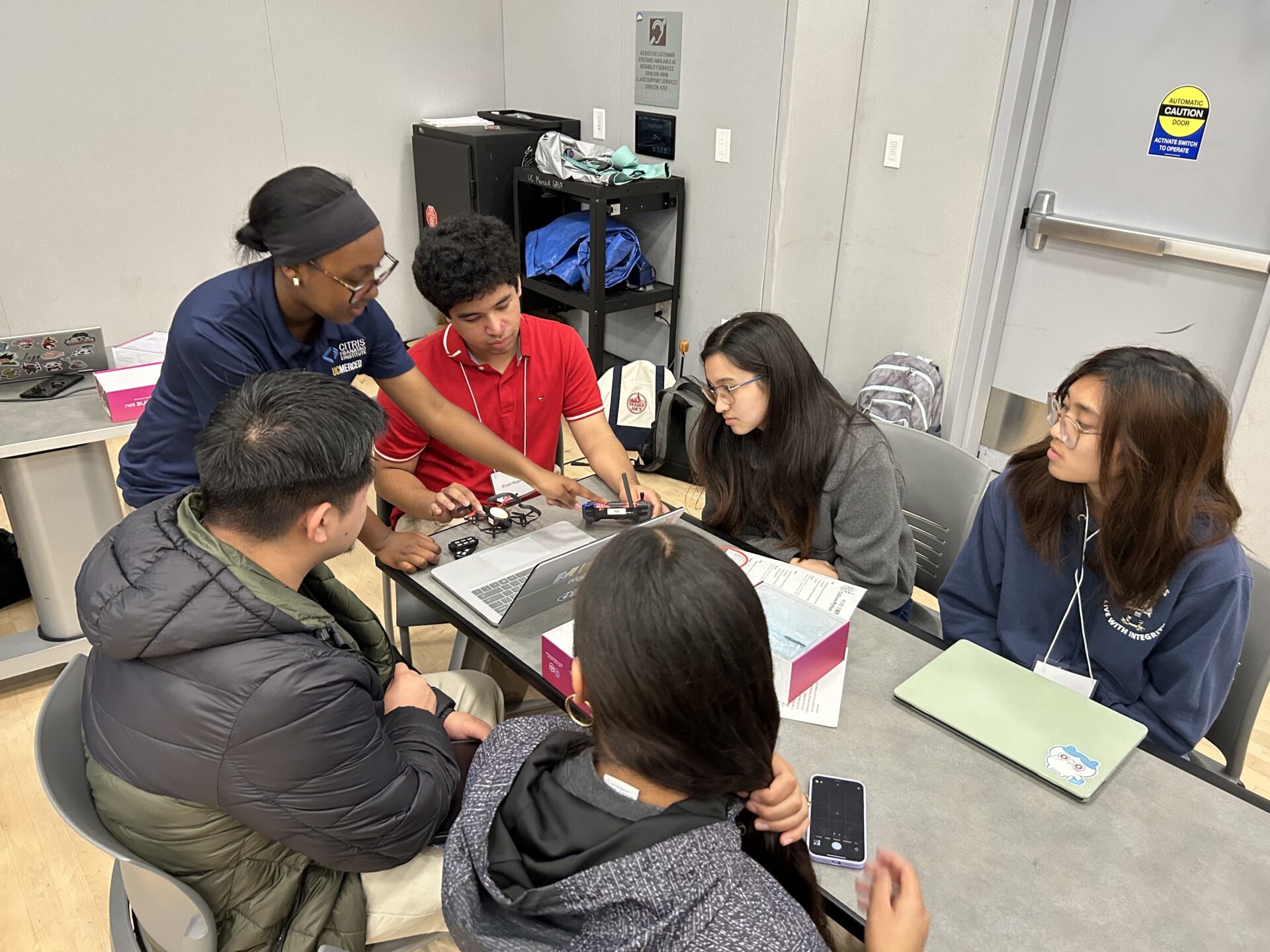 A group of 6 students sitting around a table working on a drone project