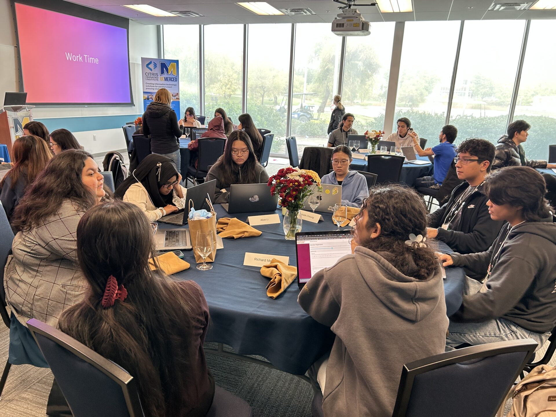 Workshop participants sitting around a round table, working and talking with a mentor