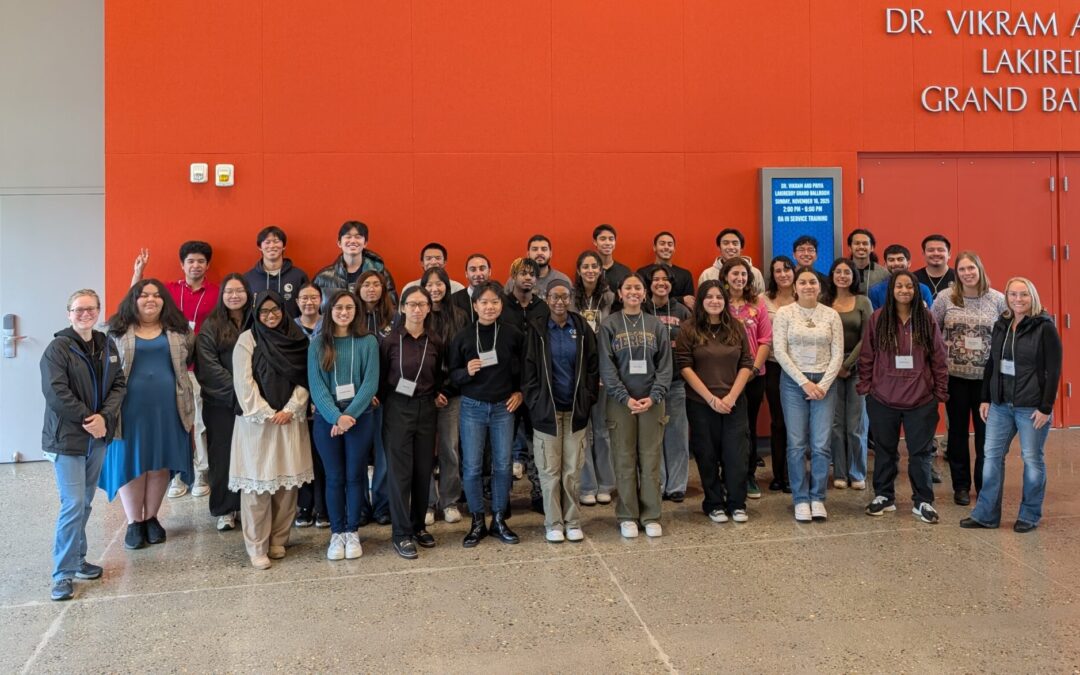 Group of 30+ student participants in Valle workshop standing in front of an orange wall posing for a group photo