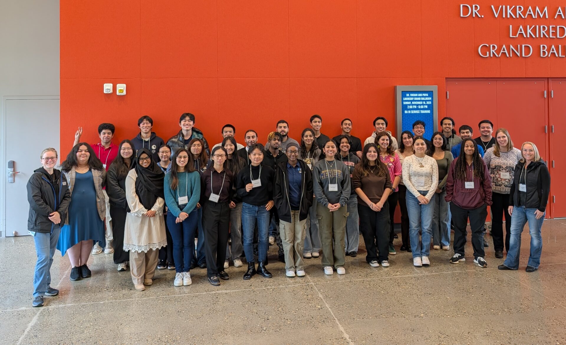 Group of 30+ student participants in Valle workshop standing in front of an orange wall posing for a group photo