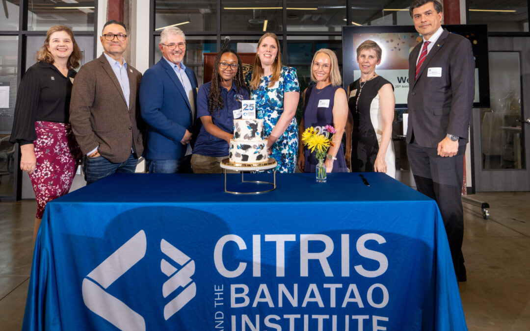 A group of 8 people in formal clothing standing behind a table with a two tier cake and flowers. The blue tablecloth reads CITRIS and the Banatao Institute.
