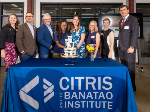 A group of 8 people in formal clothing standing behind a table with a two tier cake and flowers. The blue tablecloth reads CITRIS and the Banatao Institute.