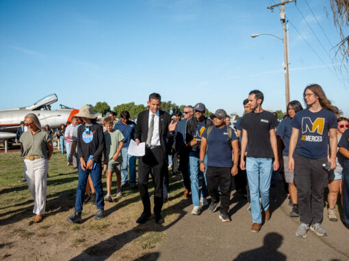NASA Administrator Jared Isaacman walks and talks with a group of UC Merced students at the Castle Air Museum, against a backdrop of airplanes